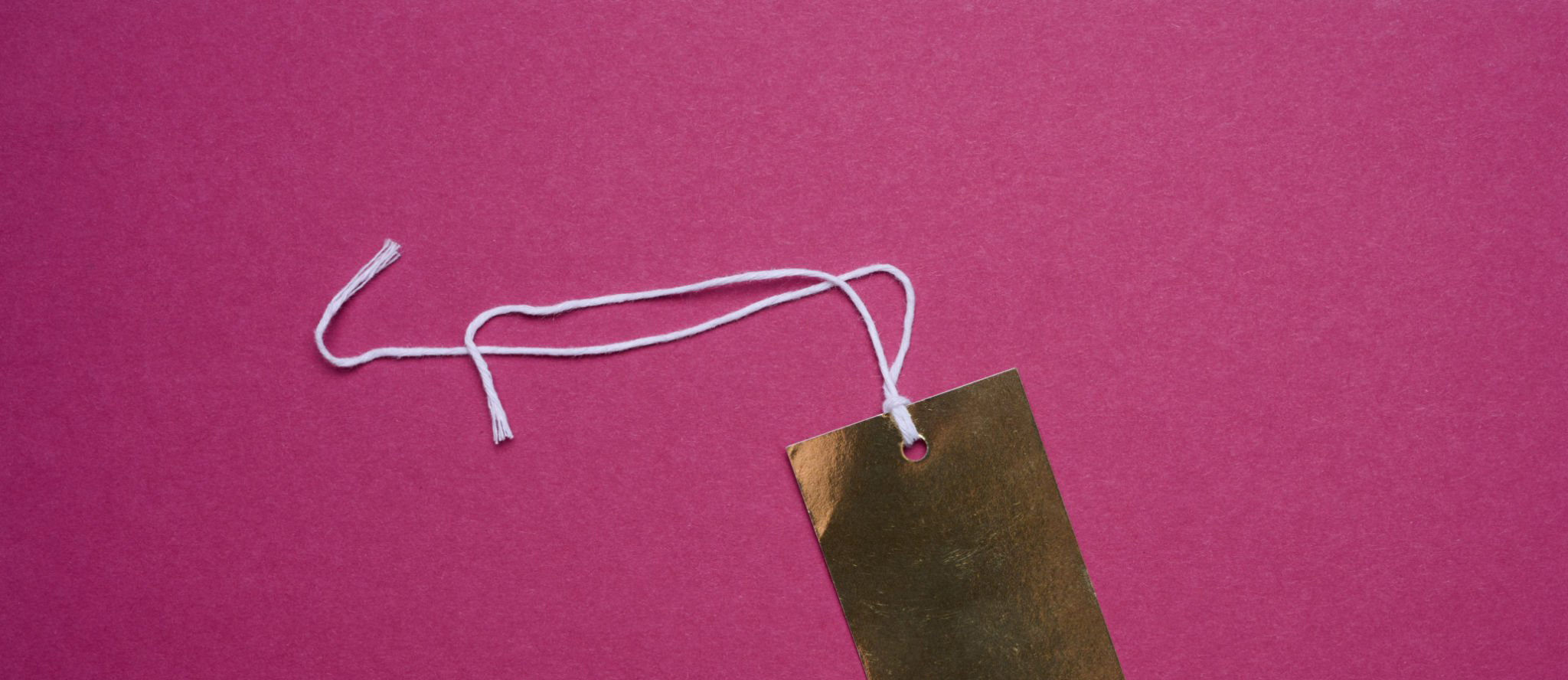 Golden price tag with a white string for clothing and merchandise on a pink background